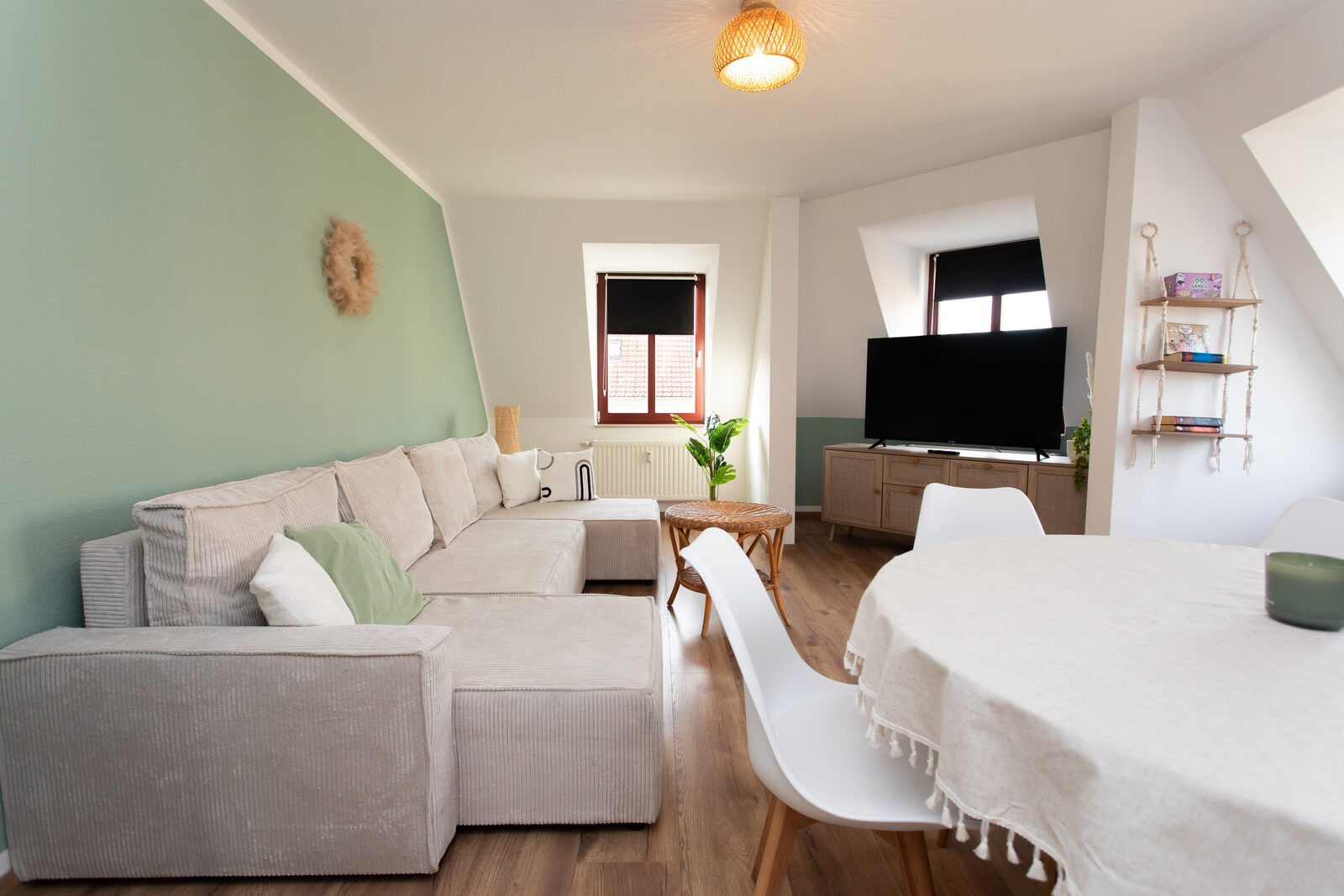 Wohnzimmer des Boho-Chic-Apartments mit salbeigrüner Wand, großem Sofa und rundem Esstisch