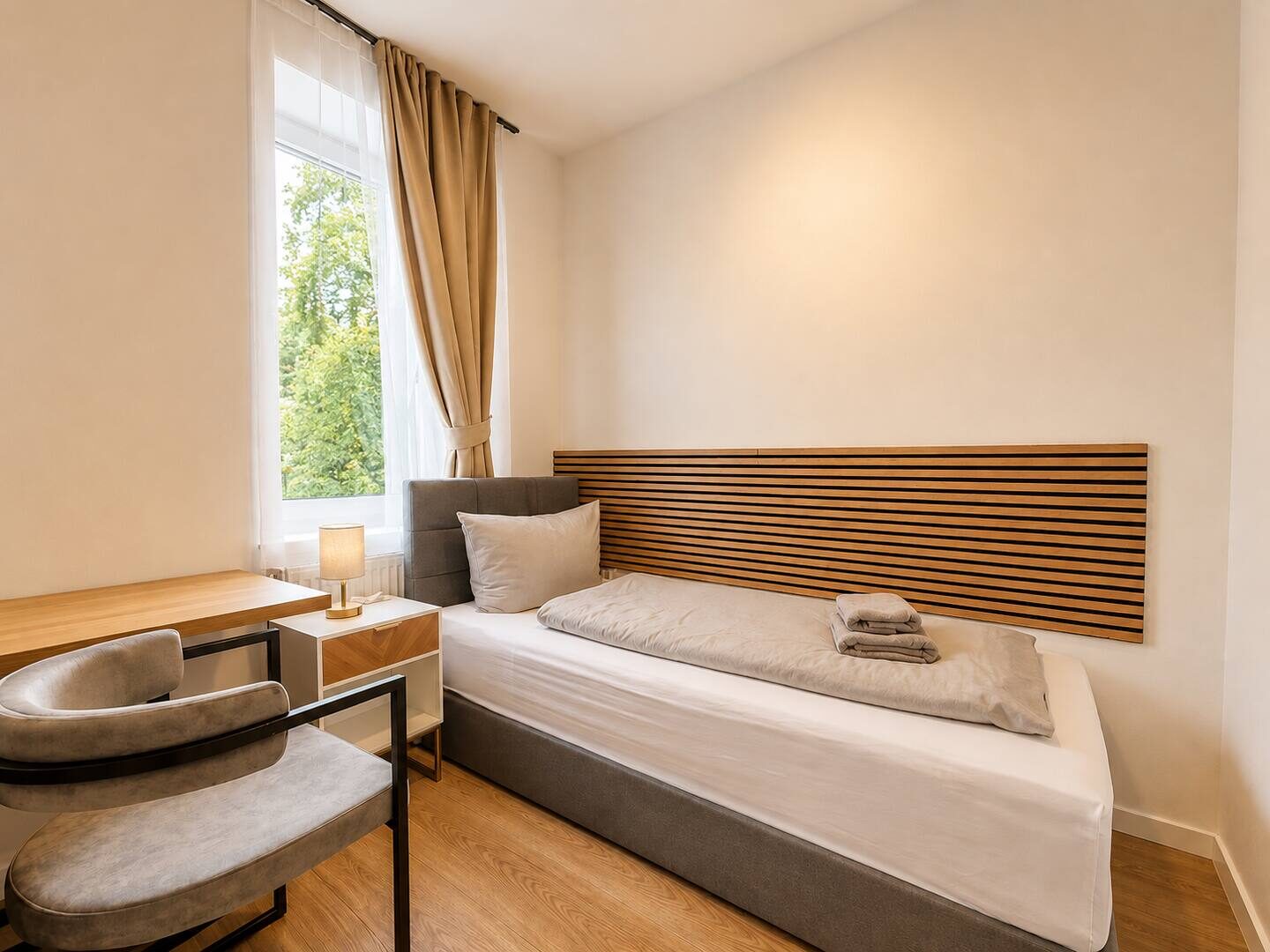 Einzelzimmer mit Bett, Holz-Lamellen-Wandpaneel und Schreibtisch am Fenster